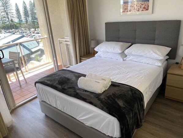 A hotel room with a bed, a bedside table, a lamp, a view of the outside, and a window. - Mooloolaba Beachfront Apartment (Mooloolaba)