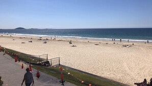 A beach with a clear sky, sandy shore, and a few people. - Mooloolaba Beachfront Apartment (Mooloolaba)