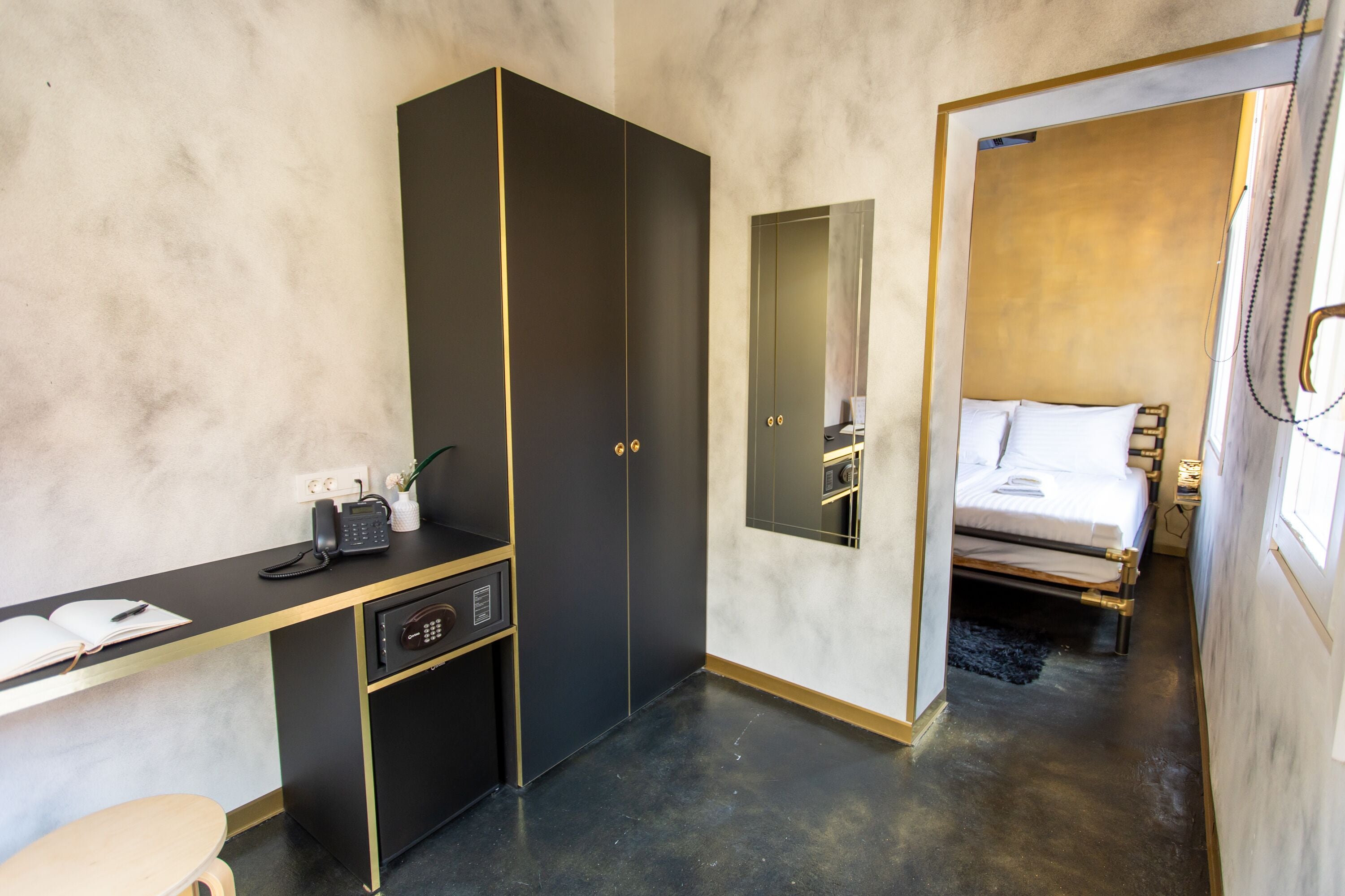 A hotel room with a desk, a wardrobe, a bed, and a mirror.