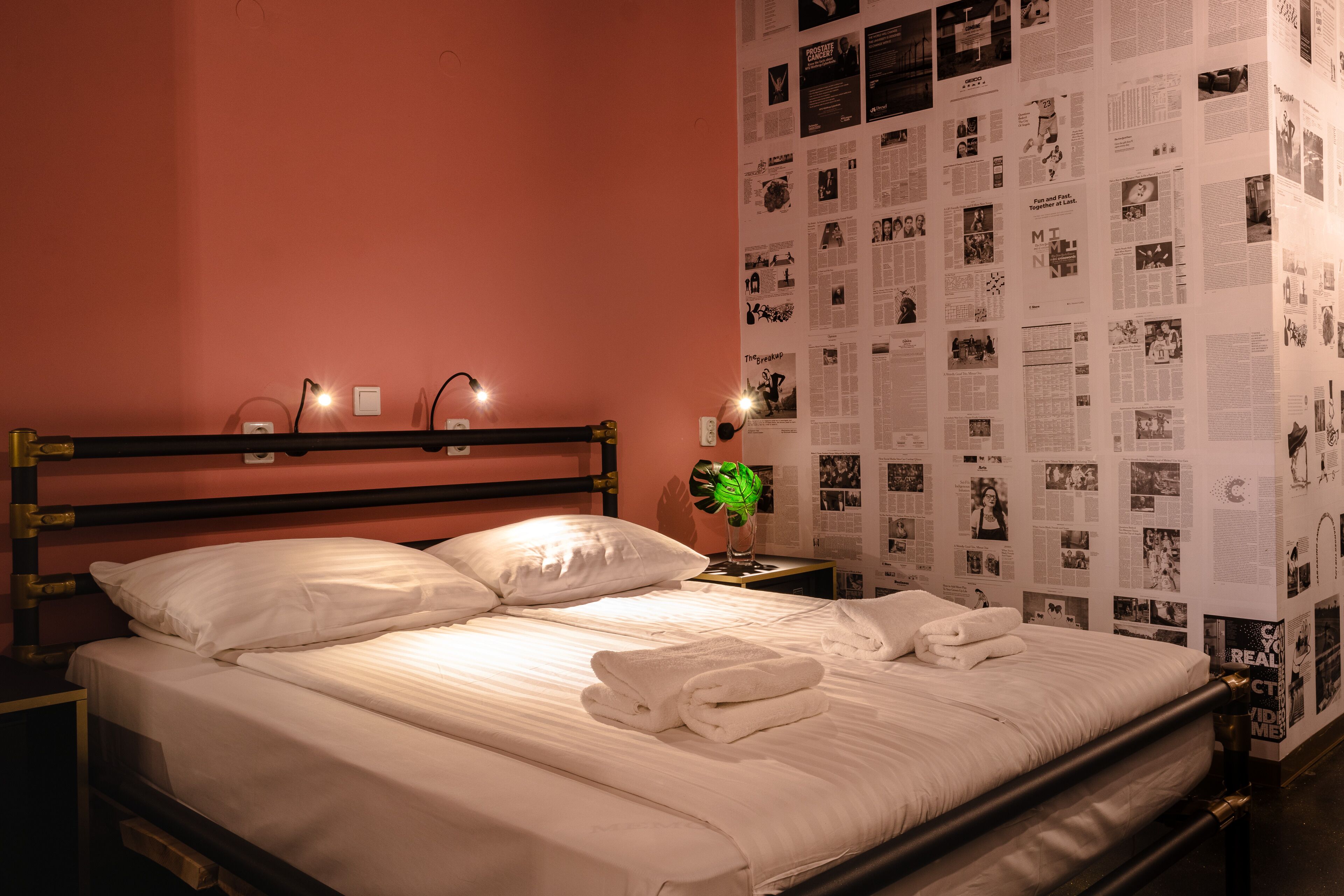 Una cama bien tendida con sábanas y toallas blancas, una mesita de noche con lámpara, y una pared decorada con imágenes impresas.