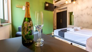 Habitación de hotel con cama, una mesa con una botella y vasos, pared verde y televisor.