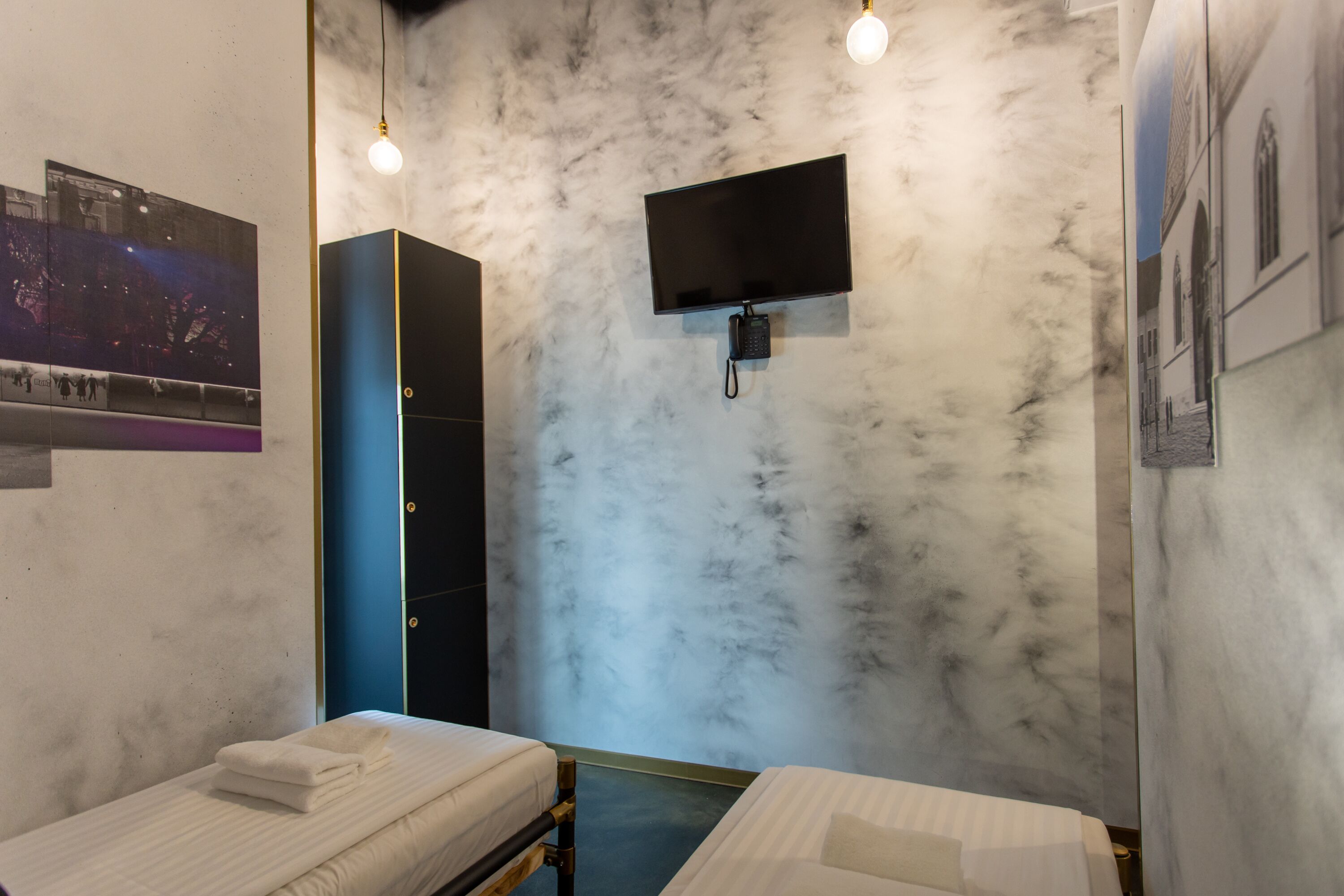 Habitación de hotel con dos camas, un televisor montado en la pared y una pared con textura similar al mármol.