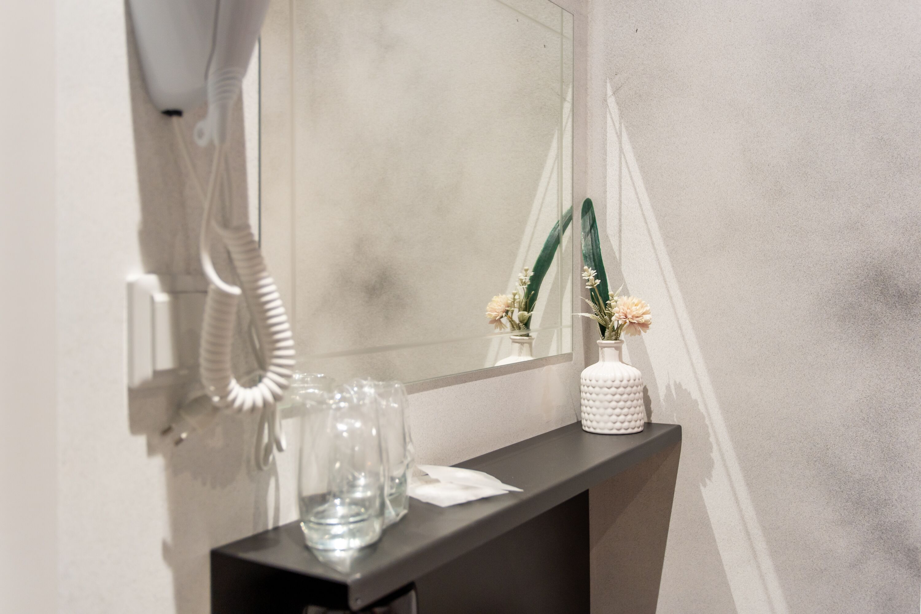 Ein Badezimmer mit Spiegel, Telefon und einer Blumenvase auf einer Ablagefläche.