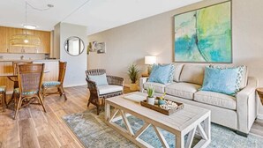Un salon comprenant un canapé, une table basse et des fauteuils. On y trouve également un coin repas avec une table et des chaises. Un ventilateur de plafond est visible.