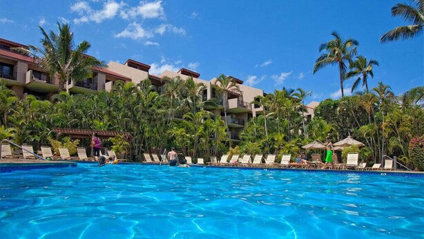 Une piscine d’hôtel avec une eau d’un bleu limpide, des palmiers et une rangée de chaises longues.