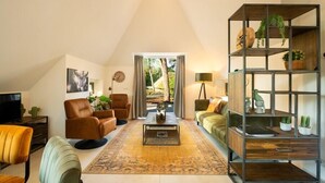 A spacious living room with a high ceiling, a large window, a sofa, a coffee table, and a bookshelf. - Sprielderbosch 17 Luxury holiday home Veluwe, located in the woods (Putten)