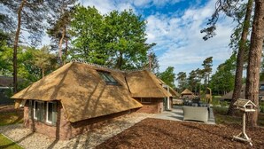 A thatched-roof house with a small attached structure, surrounded by trees and a clear sky. - Sprielderbosch 17 Luxury holiday home Veluwe, located in the woods (Putten)