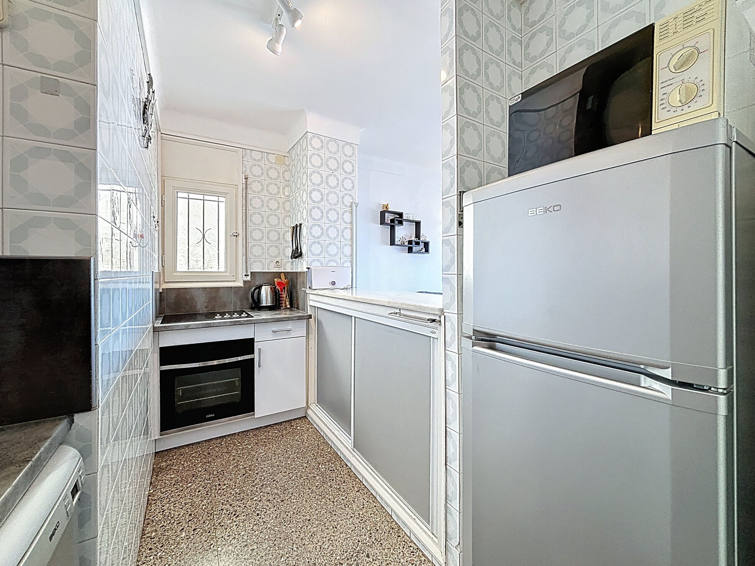 A compact kitchen with white cabinets, a built-in oven, a microwave, and a stainless steel refrigerator.