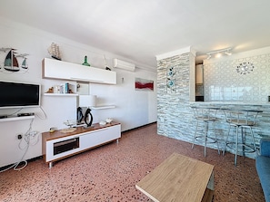 Una sala de estar moderna con televisor, estanterías y una zona de cocina con taburetes de bar.