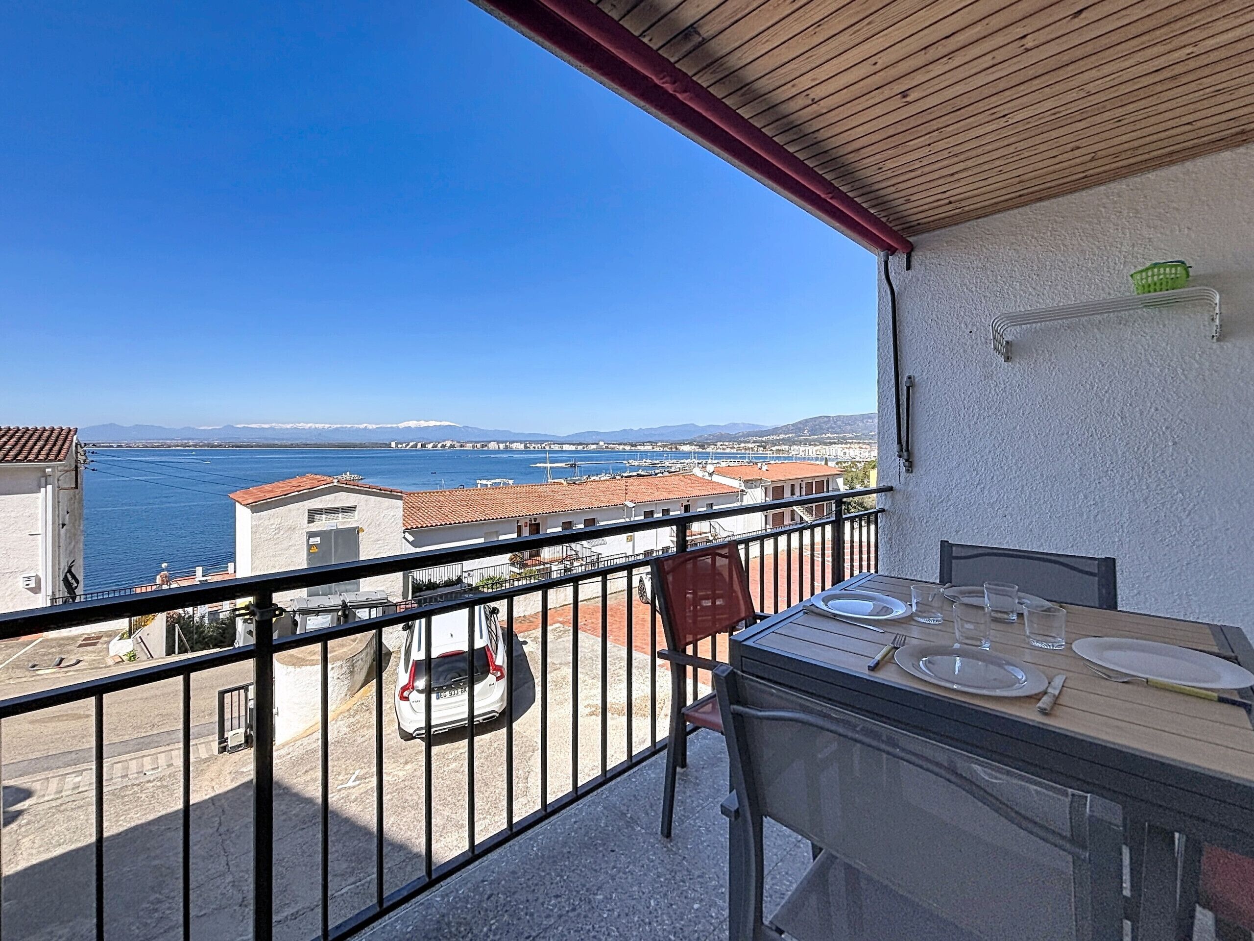 Un balcon avec une table dressée pour le dîner, offrant une vue sur la côte, avec des bâtiments et un ciel dégagé.