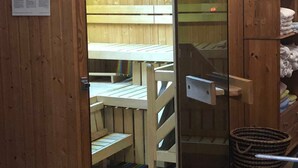 A wooden room with a wooden bench, a glass door, and a small table.