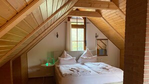 A bedroom with a sloped ceiling, a bed, a bedside table, a window, and a mirror.