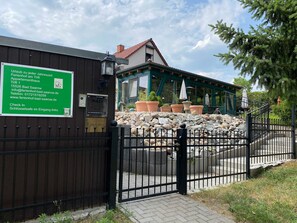 Une entrée fermée par un portail, agrémentée d’un panneau indicateur, un chemin pavé de pierres et un bâtiment doté d’un toit en tuiles.