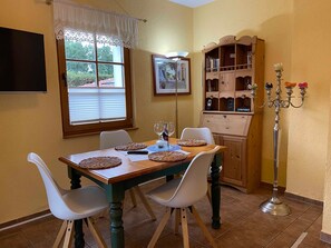 A dining area with a wooden table, white chairs, a candelabra, and a wooden cabinet with books.