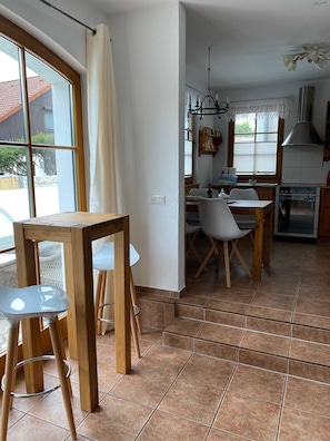 A kitchen with a stove, dining table, chairs, and a window with curtains. - Apartment No. 3 Lavender - Ferienhof am Trift (Bad Saarow)