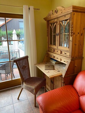 A room with a wooden cabinet, wicker chair, and a red sofa. - Apartment No. 3 Lavender - Ferienhof am Trift (Bad Saarow)