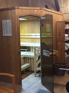 Une pièce en bois avec une table et des bancs en bois, une porte en verre et un meuble contenant des serviettes pliées.