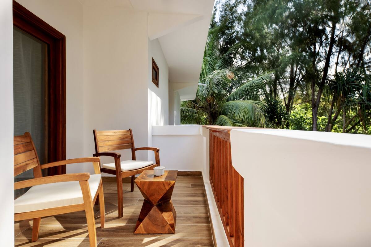 A balcony with wooden furniture, including chairs and a table, overlooking a lush green landscape.