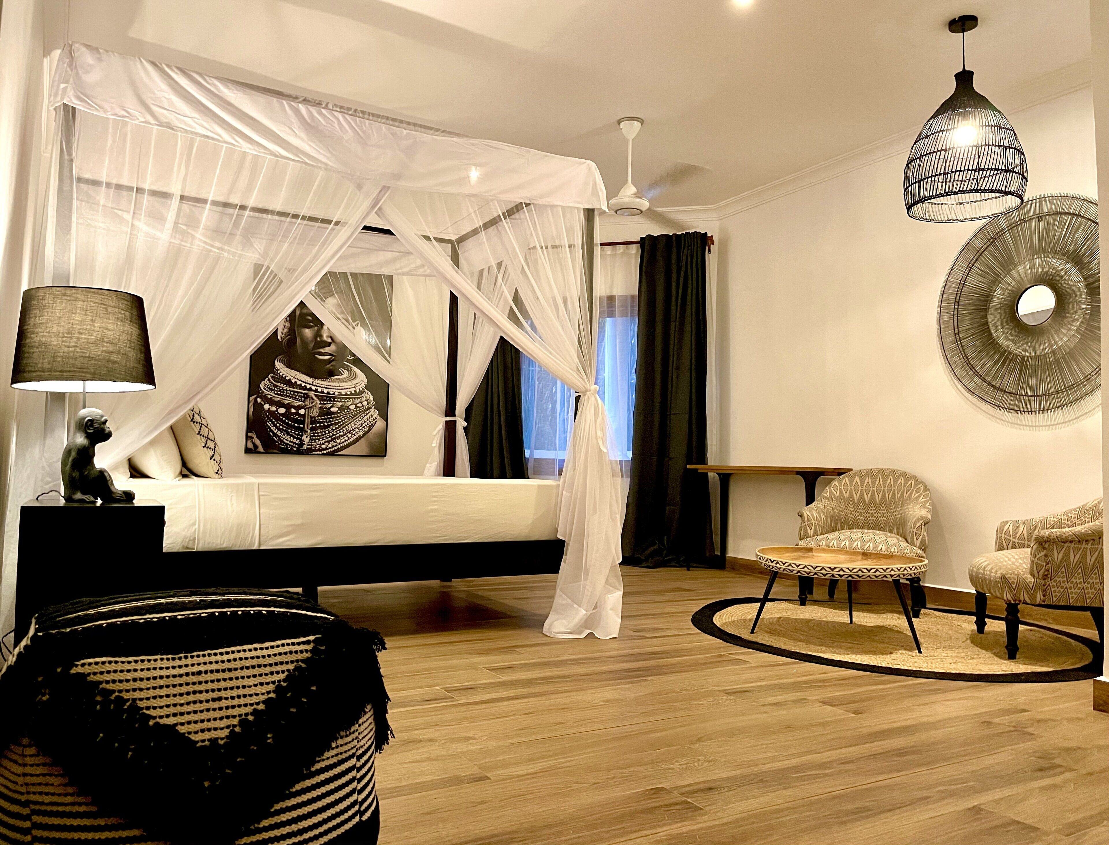 Un dormitorio con cama a dosel, lámpara de noche, una silla decorativa y una lámpara de pared.