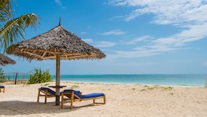 A beach with two lounge chairs under a thatched umbrella, a palm tree, and a clear blue sky. - Amani Boutique Hotel - Small Luxury Hotels of the World (Paje)
