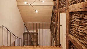 Una escalera de madera con barandilla metálica, techo de madera y pared rústica.