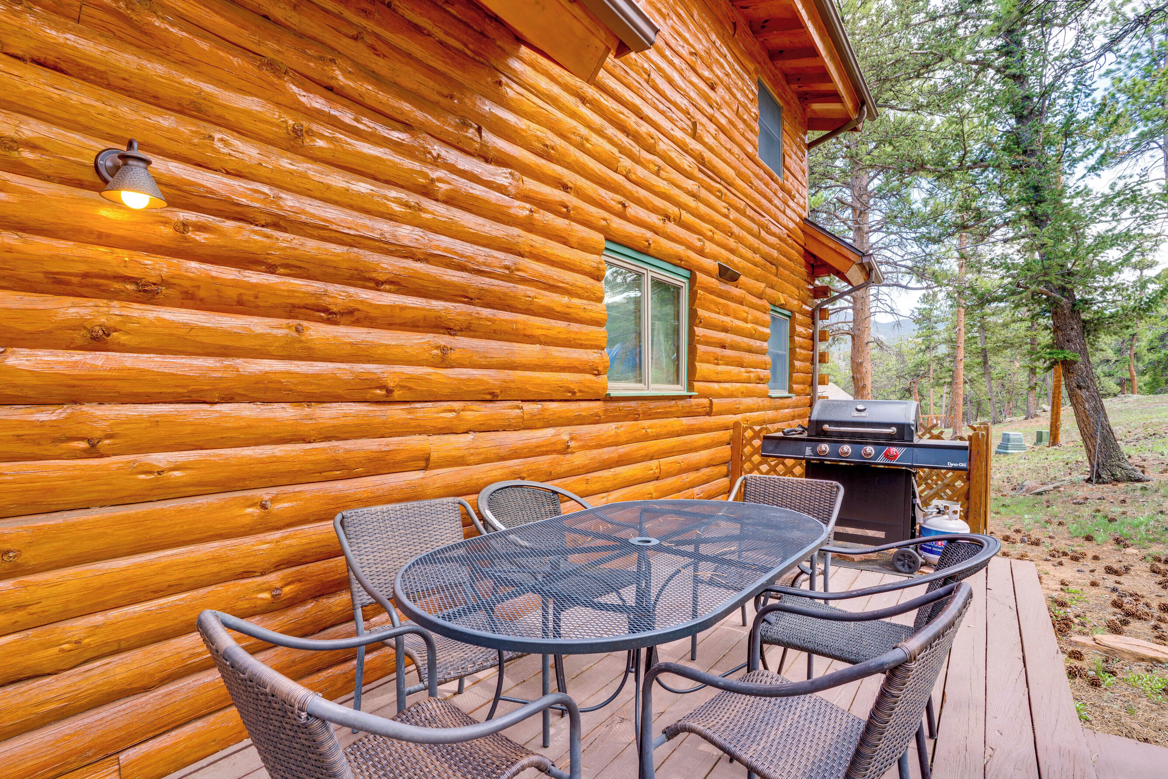 Une cabane en rondins avec une terrasse, un espace salon extérieur et un barbecue.