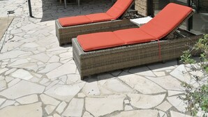Un patio con dos sillones de mimbre con cojines rojos, una mesa y sillas bajo un gran paraguas.