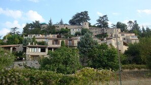 Un pueblo en una ladera con edificios de piedra, algunos con balcones, y una imponente estructura de torre.