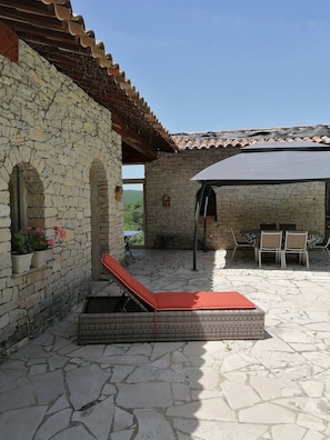 A stone patio with a red lounge chair, a covered outdoor seating area, and a stone wall with windows. - 🌿 Dry stone summer house with private pool - Lincel, Provence (Lincel)