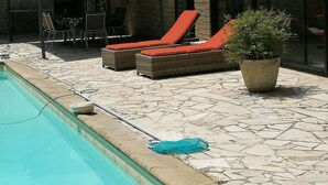 Un área de piscina con sillones reclinables y una zona de estar cubierta.