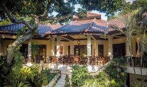 A traditional villa with a tiled roof, a covered patio with wooden furniture, and a stone staircase leading to the entrance.