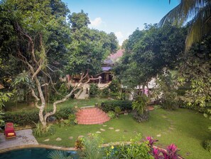 A lush garden with a swimming pool, a stone staircase, and a building with a red roof.