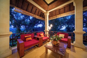 A covered outdoor seating area with wooden furniture and a view of trees.
