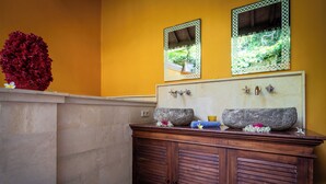 Un baño con tocador de madera, dos espejos y un coral rojo decorativo.