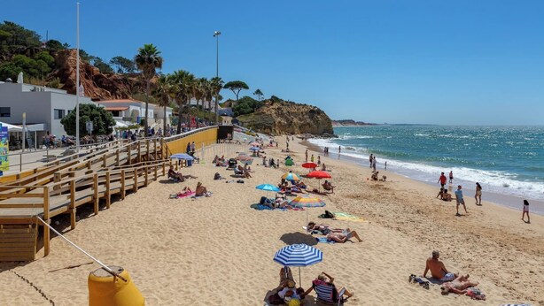 Una playa con asientos de madera, sombrillas y gente tomando el sol.