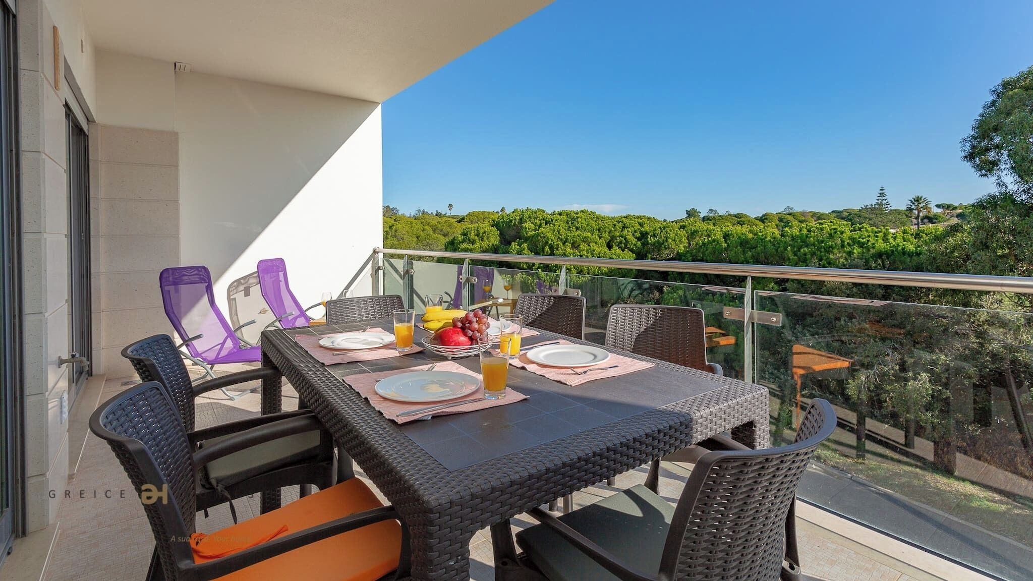 Ein Balkon mit Tisch, gedeckt für das Frühstück, inklusive Tellern, Besteck und einer Obstschale.