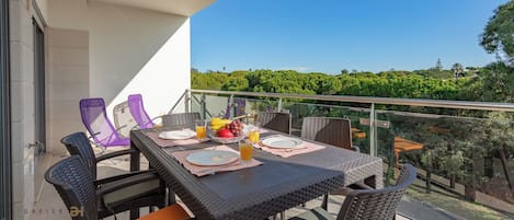 En balkon med et bord dækket til morgenmad, inklusive tallerkener, bestik og en skål med frugt.
