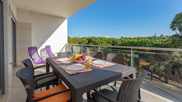 A balcony with a table set for breakfast, including plates, cutlery, and a fruit bowl.