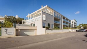 Un edificio moderno de varios pisos con balcones, un estacionamiento y un cielo despejado.