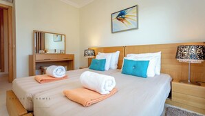 Una habitación de hotel con una cama grande, dos mesitas de noche, un cabecero de madera, un espejo, un cuadro y un área de baño con toallero.