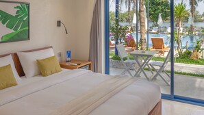 Une chambre d’hôtel avec un lit, une table de chevet, une table et une vue sur une piscine et des palmiers.