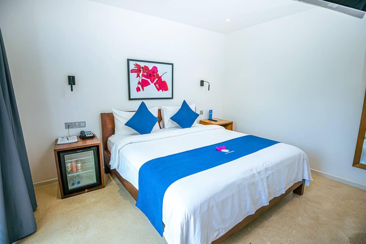 A hotel room with a bed, a nightstand, a mini-fridge, a wall-mounted artwork, and a power outlet.