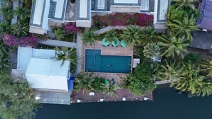 Vue aérienne d’un complexe hôtelier doté d’une piscine, entourée de palmiers et de bougainvilliers.