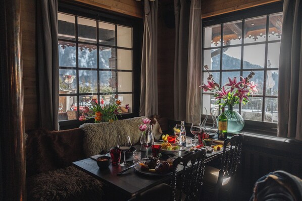 Un comedor con una mesa dispuesta para una comida, un banco cubierto de pieles y una ventana con vistas a una montaña.