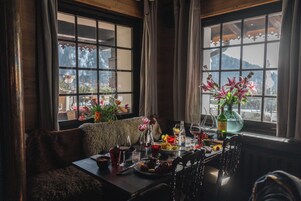 Un comedor con una mesa dispuesta para una comida, un banco cubierto de pieles y una ventana con vistas a una montaña.