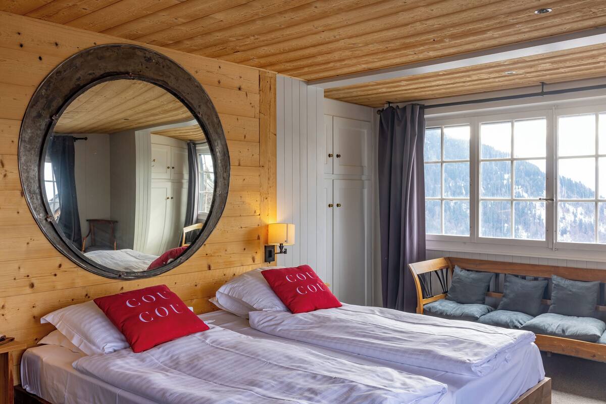 Een kamer met twee bedden, een grote spiegel en een raam met uitzicht op bergen.