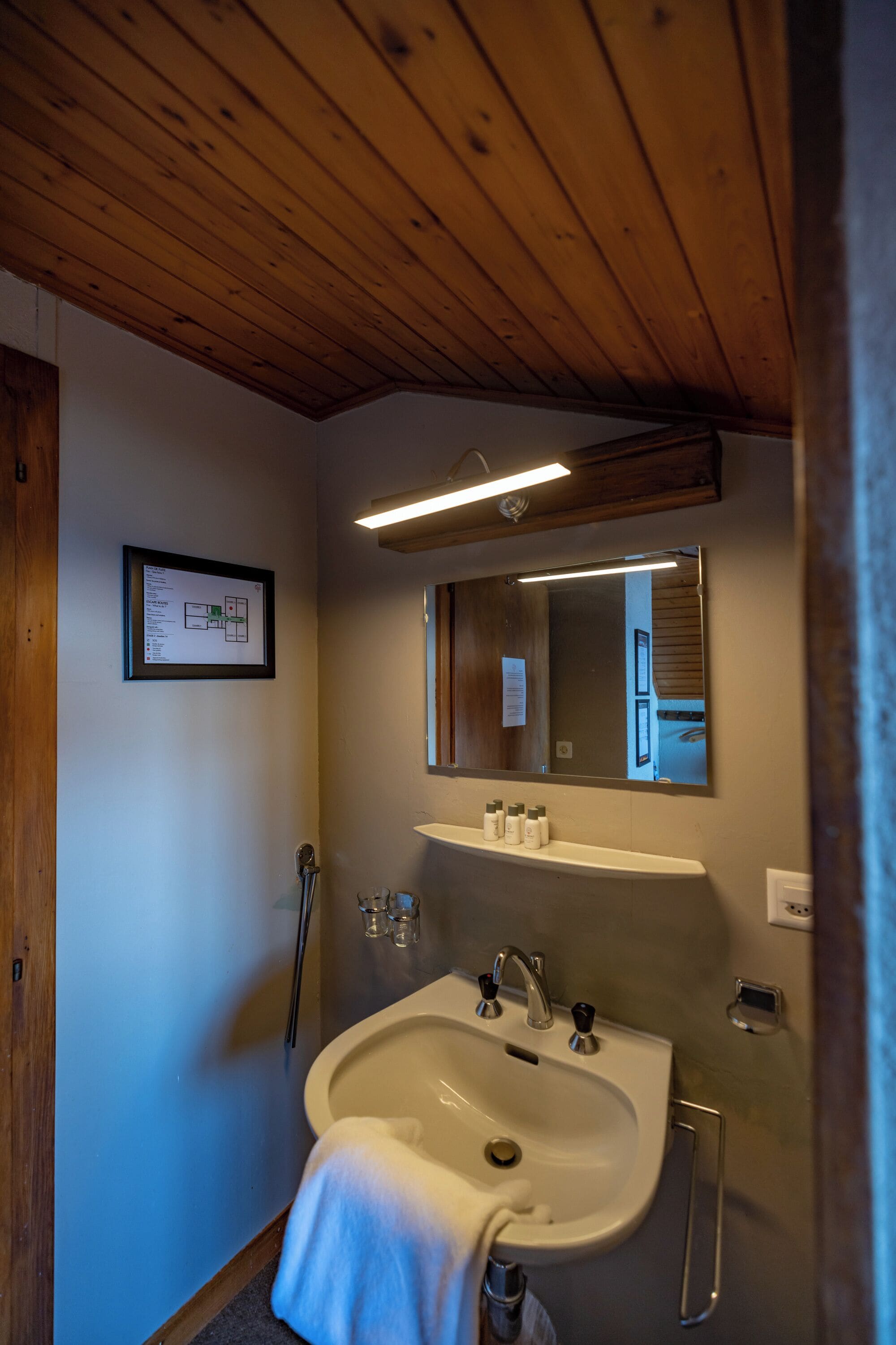 A bathroom with a wooden ceiling, a white sink with a mirror above it, and a framed map on the wall.