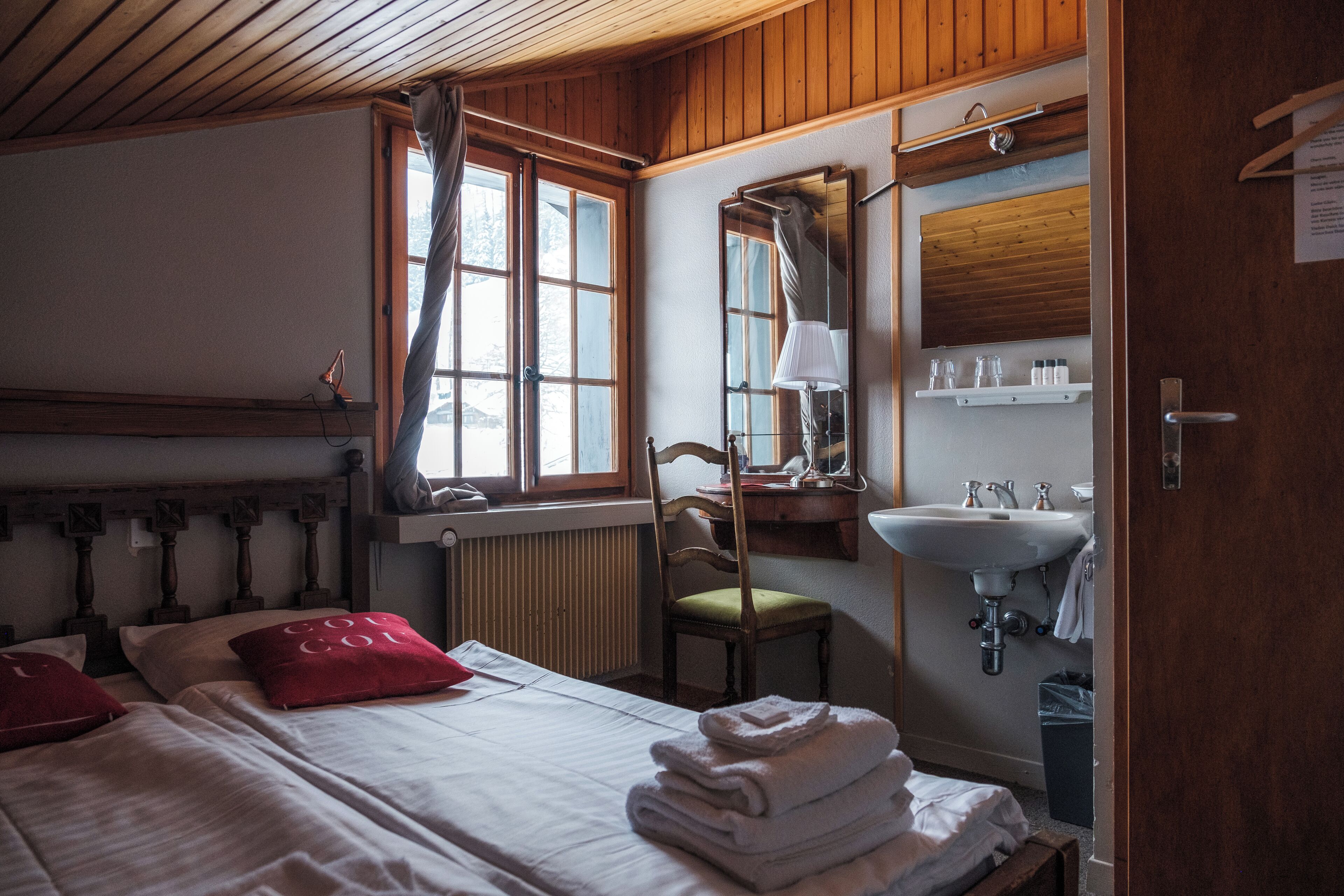 A room with a bed, a chair, a window with curtains, a mirror, a sink, and a radiator.