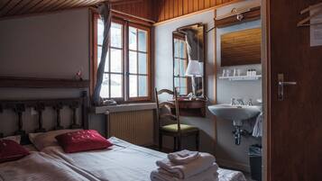 A room with a bed, a chair, a window with curtains, a mirror, a sink, and a radiator.