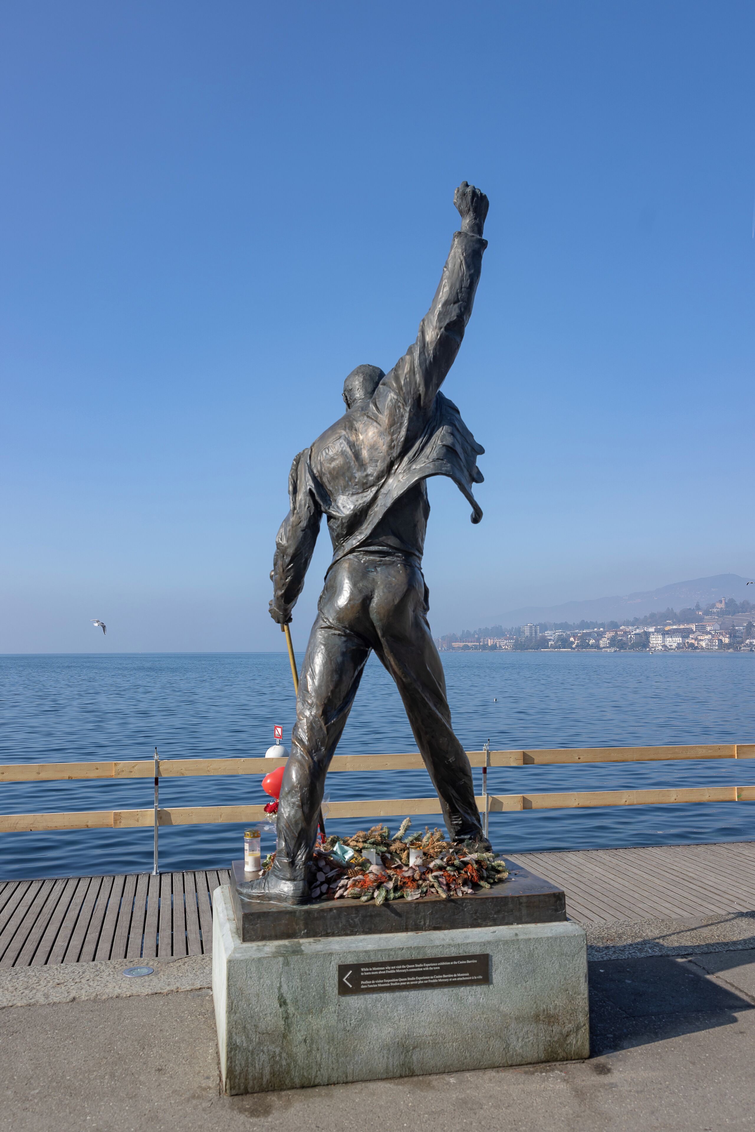 Une statue d’un homme les bras levés, debout sur une plateforme au bord de l’eau.